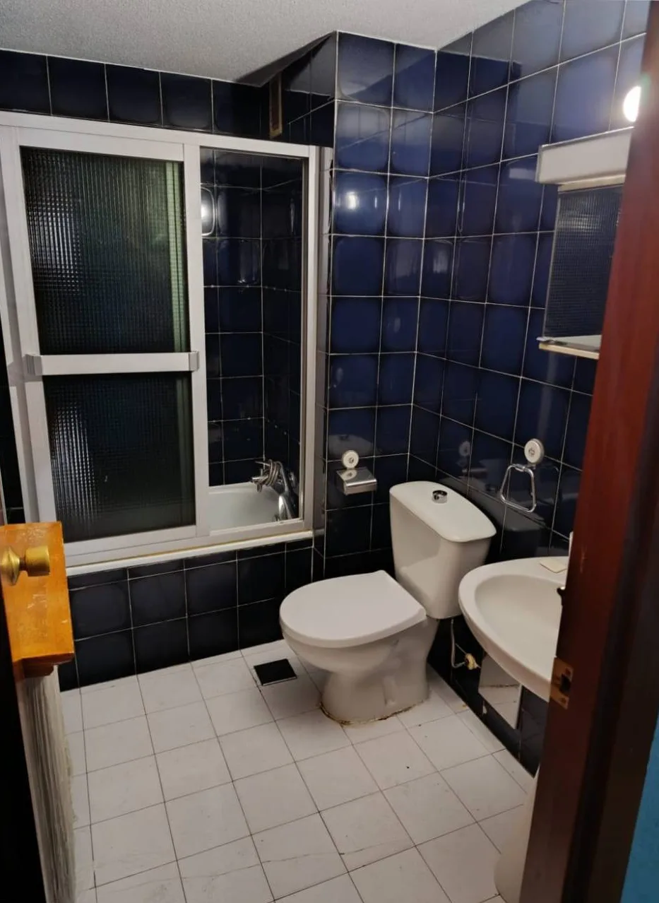 Baño antes de la reforma, con azulejo azul marino, bañera con mampara de aluminio y suelo blanco