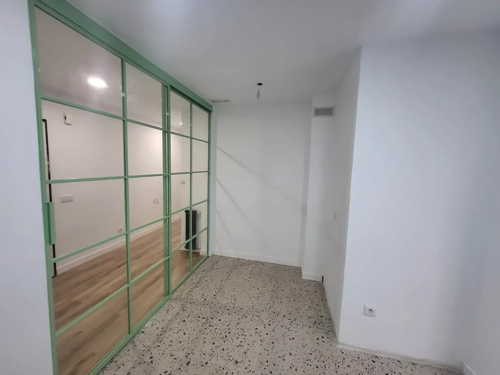 Cerramiento de cristal con perfilería verde entre el salón y la cocina