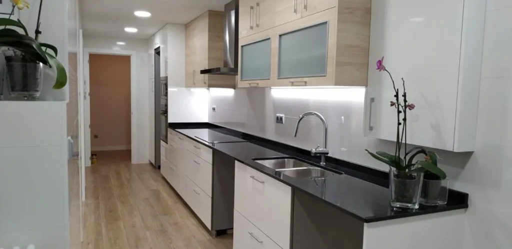 Cocina en línea reformada con muebles blancos y de madera, encimera negra y suelo de madera