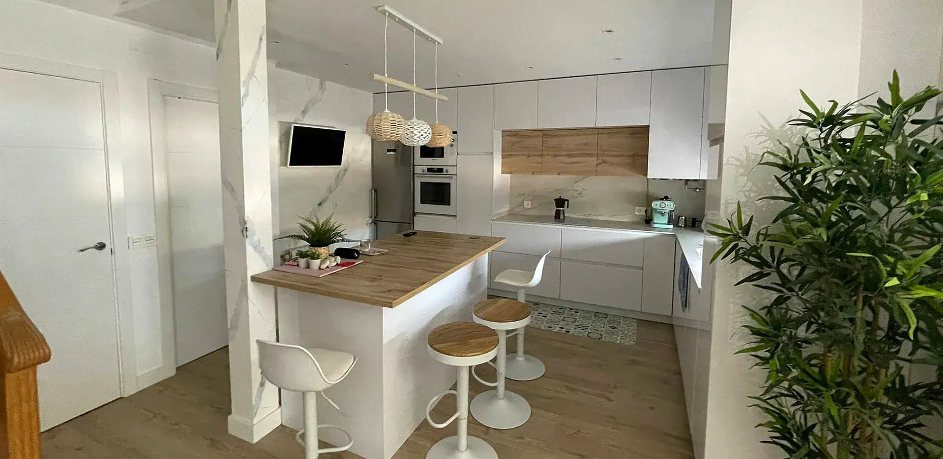 Cocina reformada por Foydecor con muebles blancos sin tirador, isla con encimera de madera y lámparas colgantes