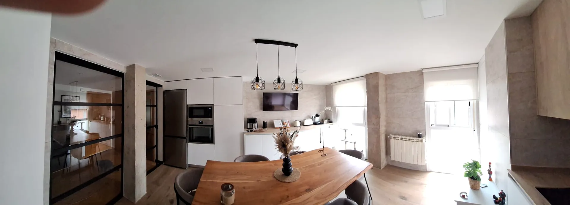 Cocina y comedor con mesa de madera, columna de hornos y frigorífico
