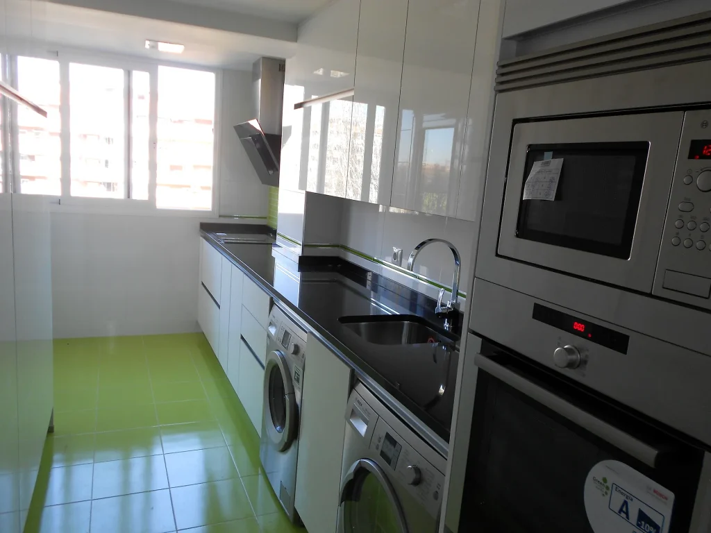 Cocina en paralelo con muebles blancos brillo, encimera negra y suelo verde