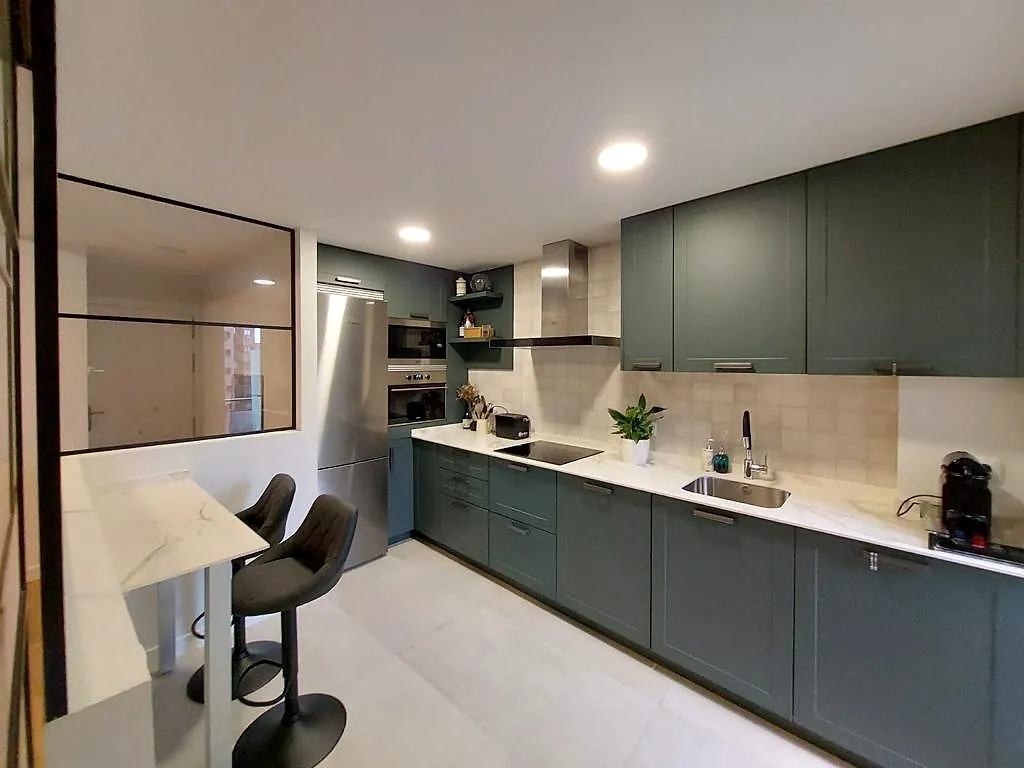 Cocina con muebles verdes, encimera blanca y barra con taburetes, en Fuente Cisneros (Alcorcón)