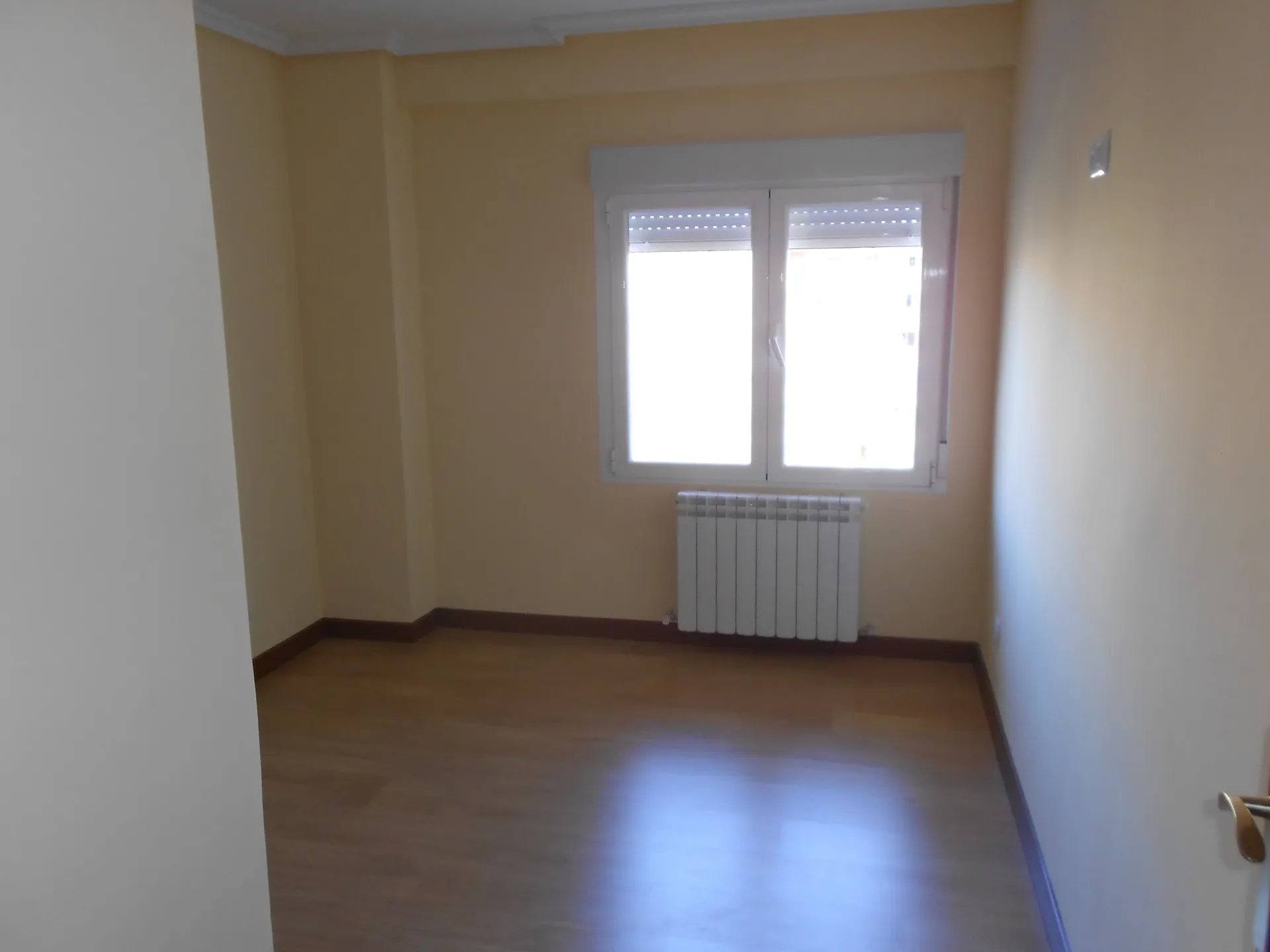 Dormitorio reformado con suelo laminado nuevo, paredes pintadas y radiador bajo la ventana