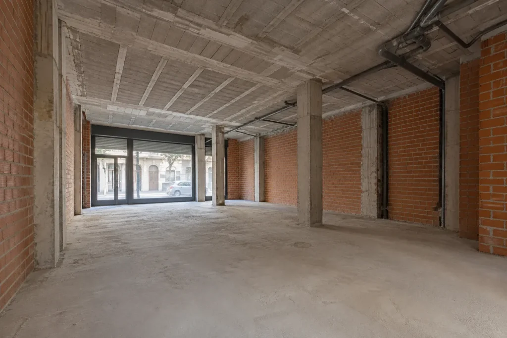 Local en bruto, con paredes de ladrillo, pilares de hormigón e instalaciones vistas, antes de la reforma