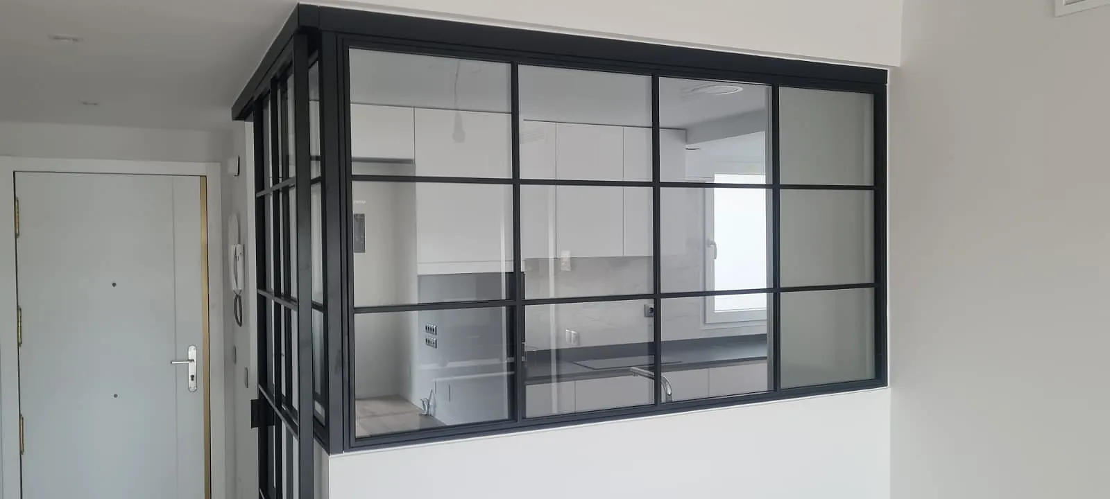 Cerramiento de cristal con barrotillo negro entre la cocina y la entrada en una reforma integral en Alcorcón