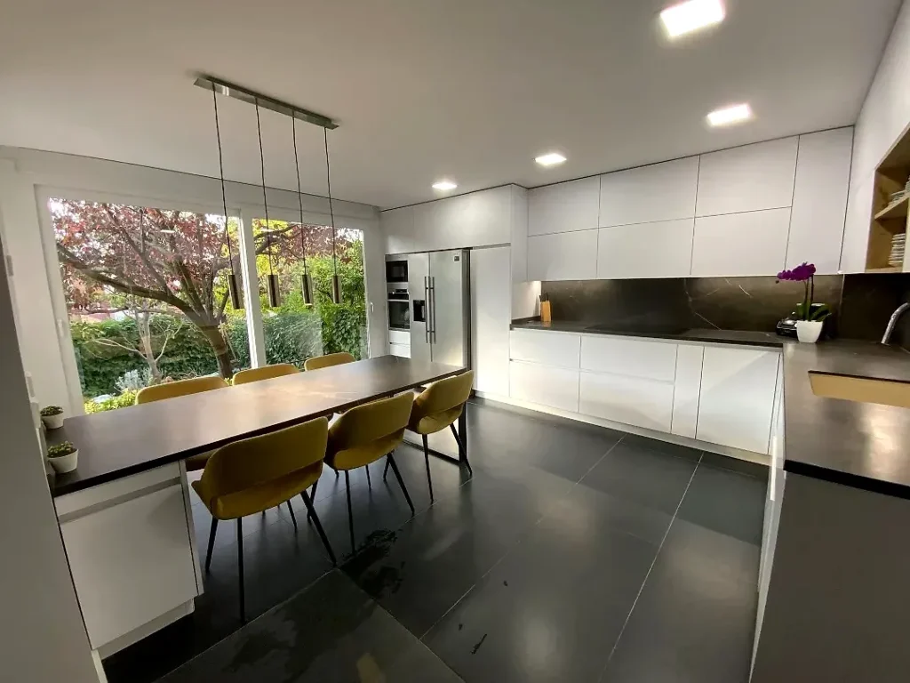 Reforma integral con cocina abierta al comedor, muebles blancos sin tirador, encimera oscura y ventanal al jardín